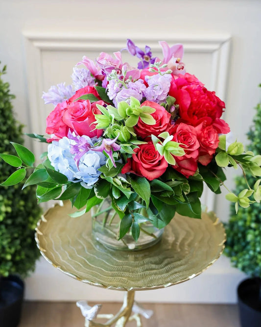 Bouquet of colorful flowers in a clear vase on a decorative table with a white wall background.